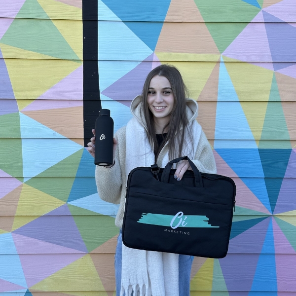 Young woman holding a water bottle and marketing bag in front of colorful geometric mural | GPS: 49.284922, -122.621562