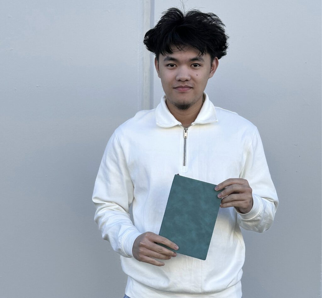 young man holding green notebook in white jacket oi marketing